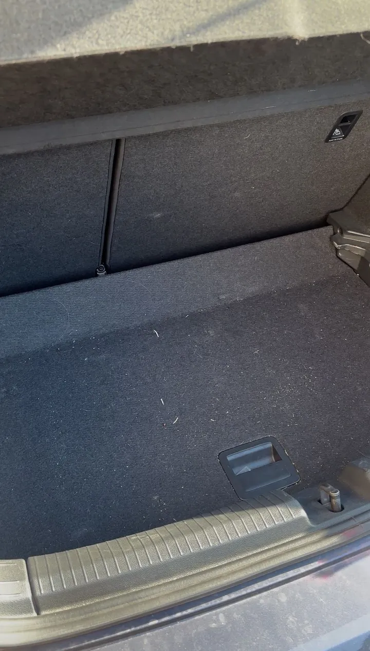 Coffre de citadine avant nettoyage : moquette poussiéreuse